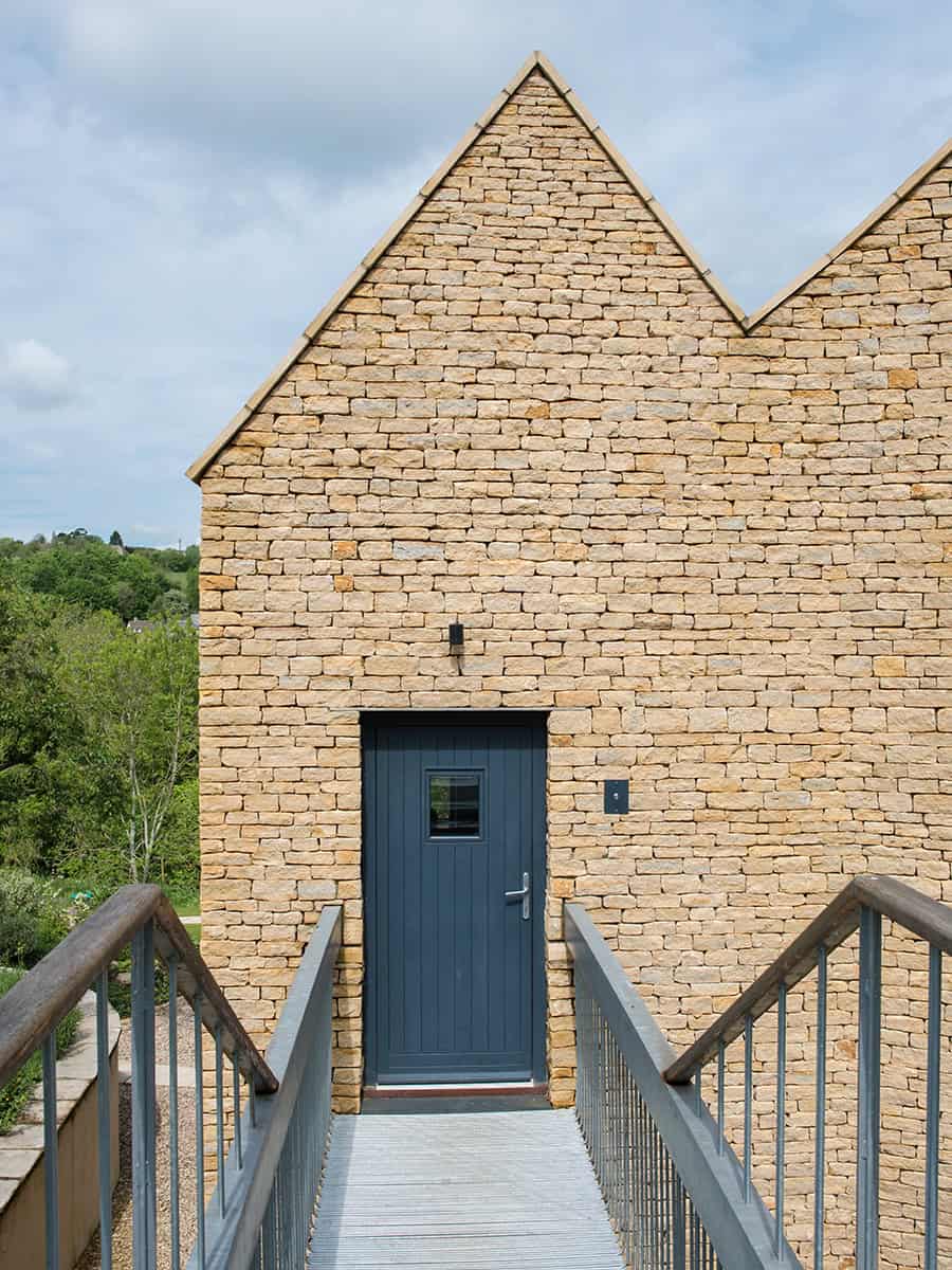 Harleywood House Cotswold stone gable entrance with metal bridge walkway and grey door
